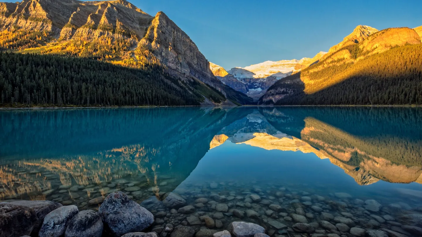 Lake Louise reflecting surrounding Rocky Mountain peaks and Victoria Glacier in warm low-angle light