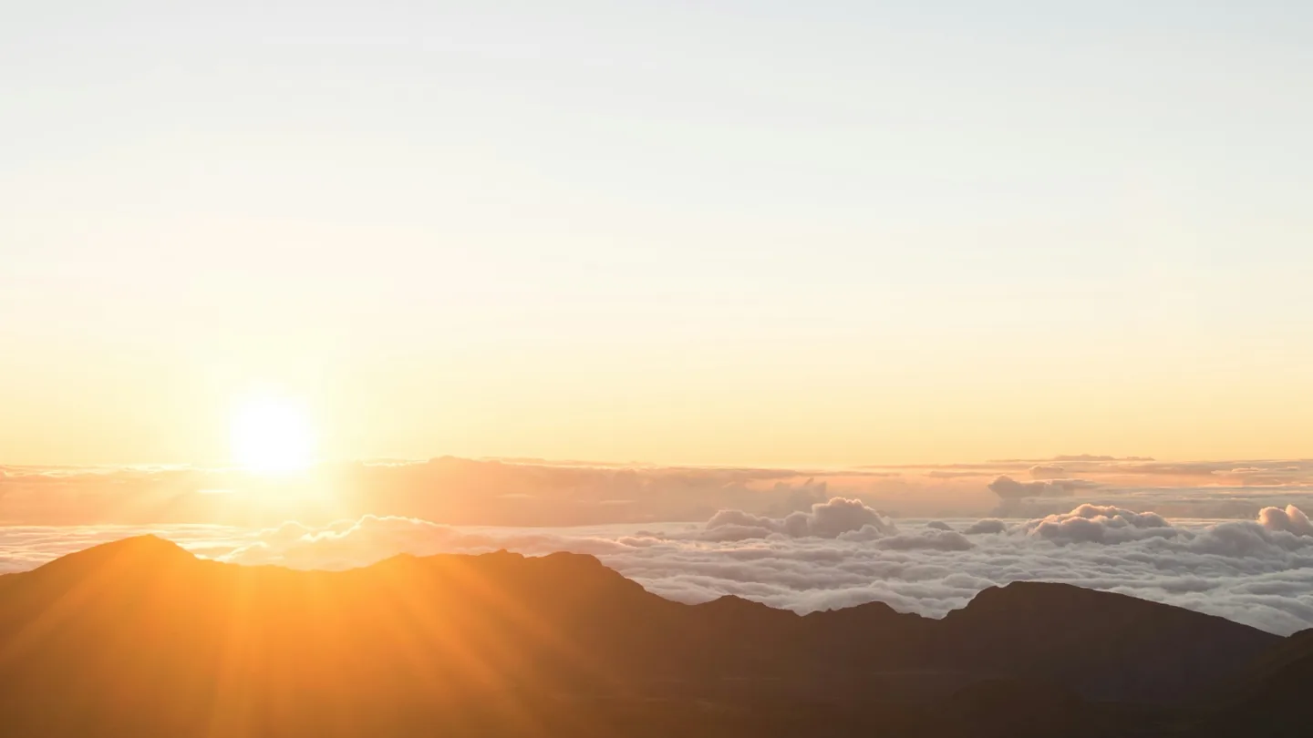 Sunrise illuminating Haleakalā volcanic ridges above a broad cloud deck