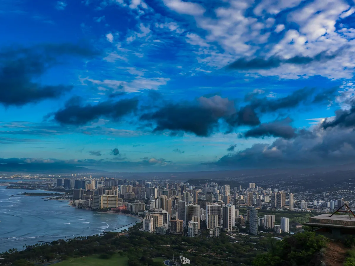 Honolulu and Waikīkī coastline beneath a deep blue sky and dramatic tropical clouds