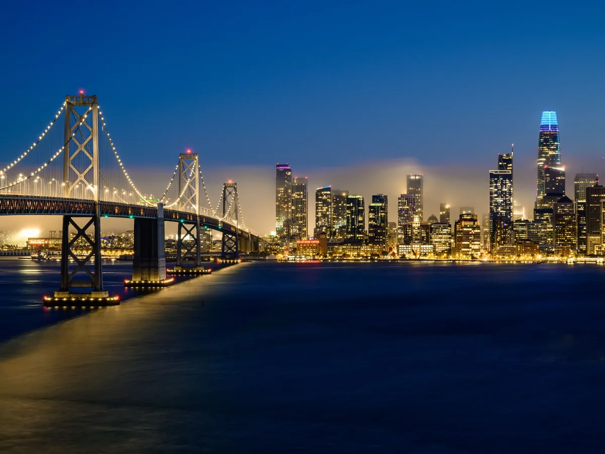 San Francisco Bay Bridge and illuminated skyline beneath a deep blue evening sky