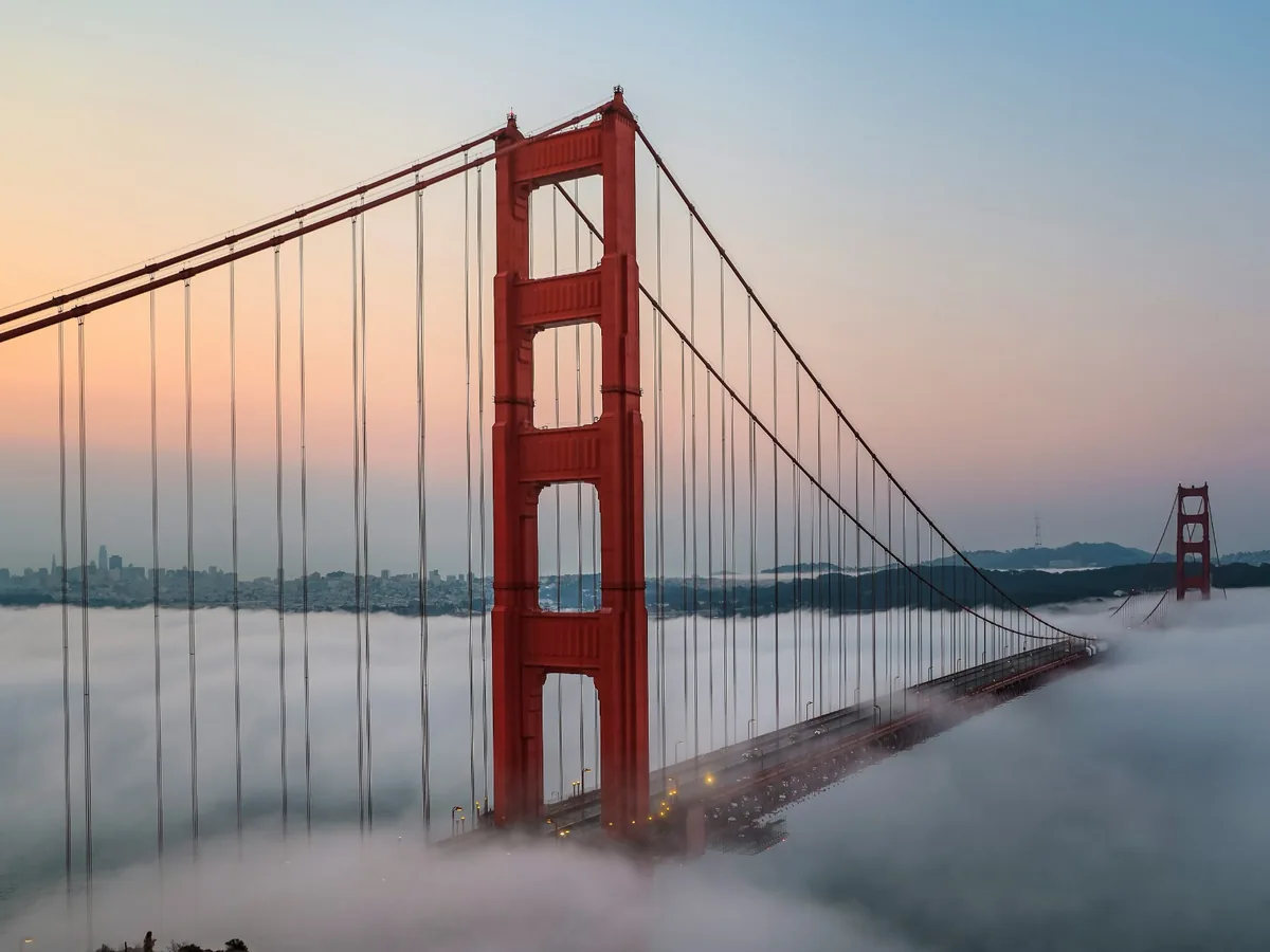 Golden Gate Bridge towers emerging above coastal fog at sunset