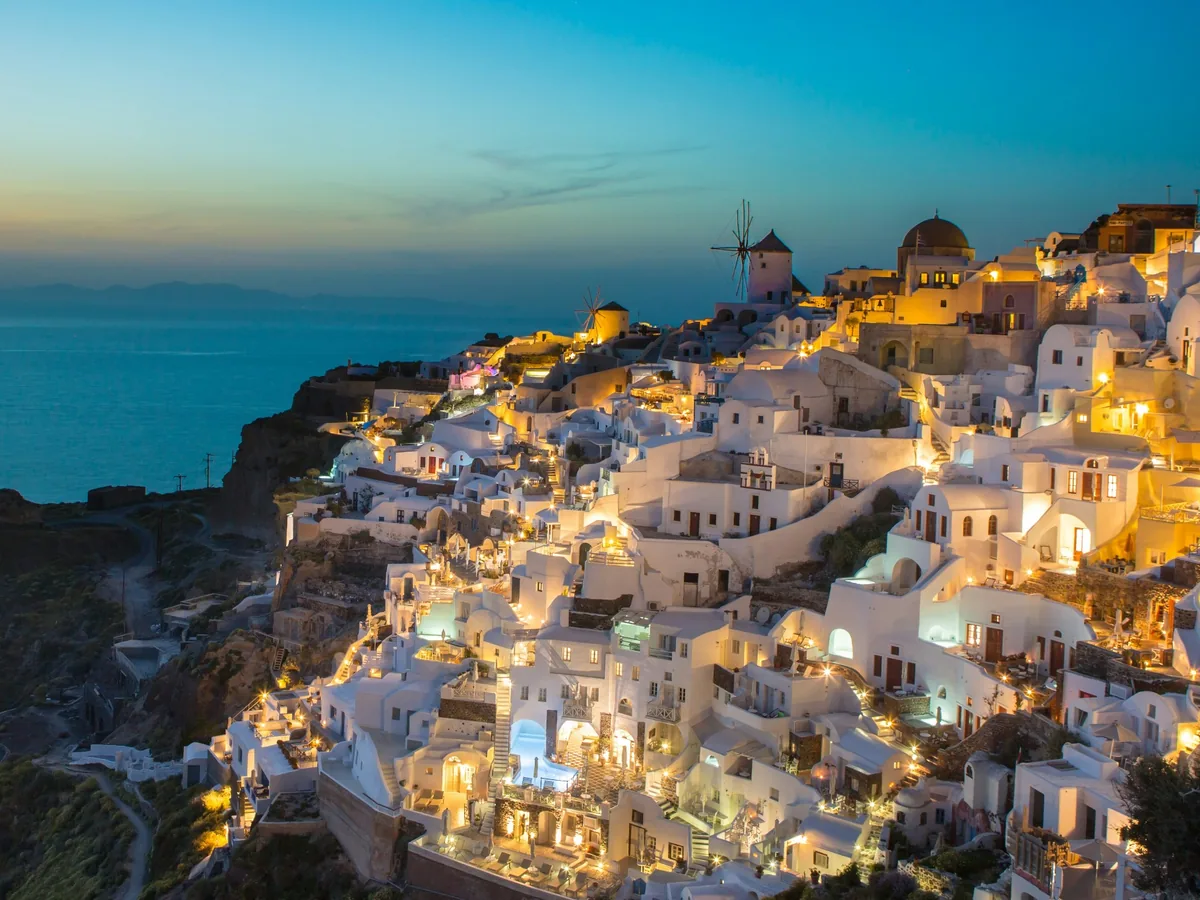Oia's whitewashed cliffside village illuminated during blue hour above the Aegean Sea