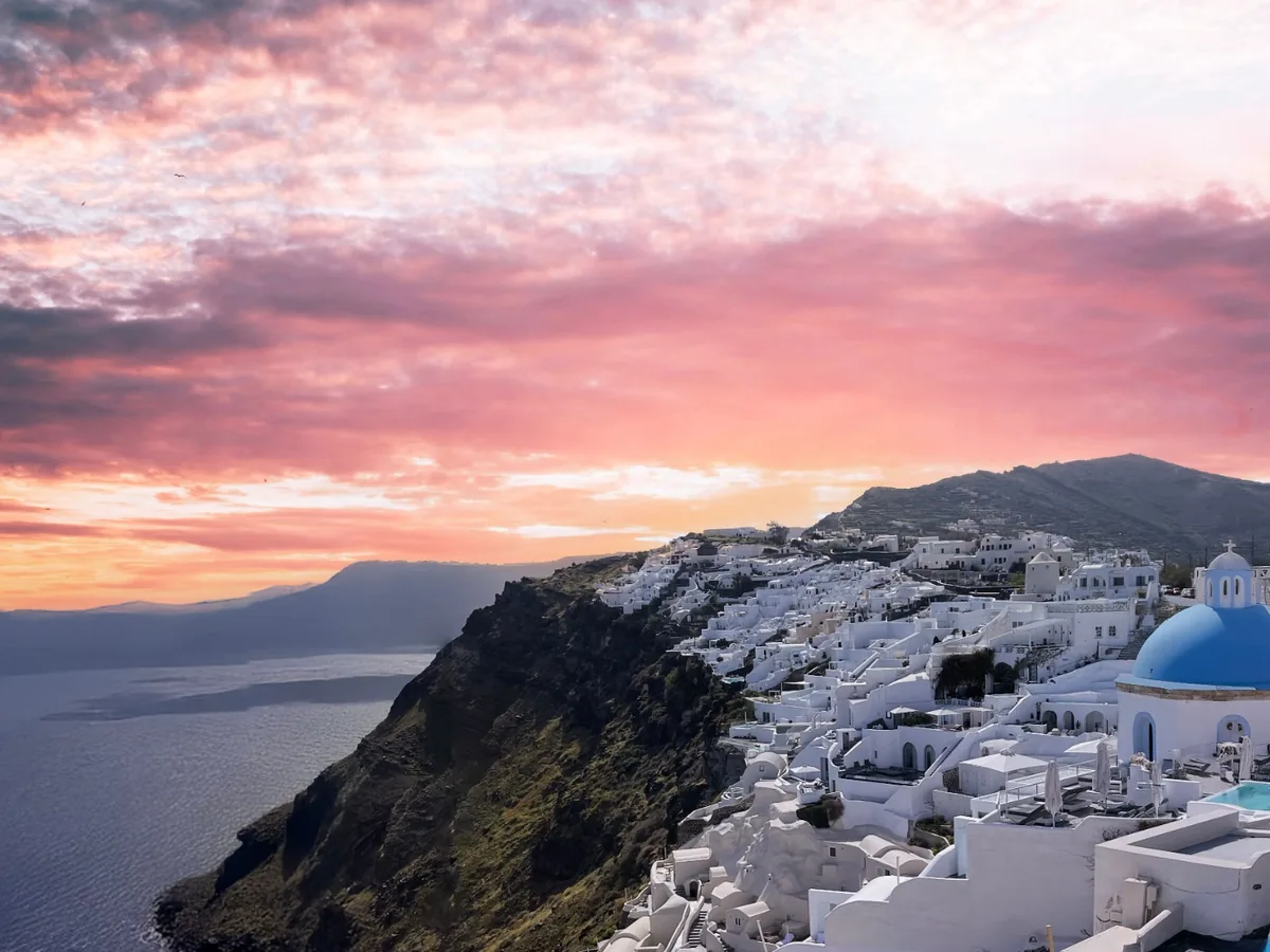Blue-domed churches and whitewashed buildings in Oia beneath colorful sunset clouds over the Santorini caldera