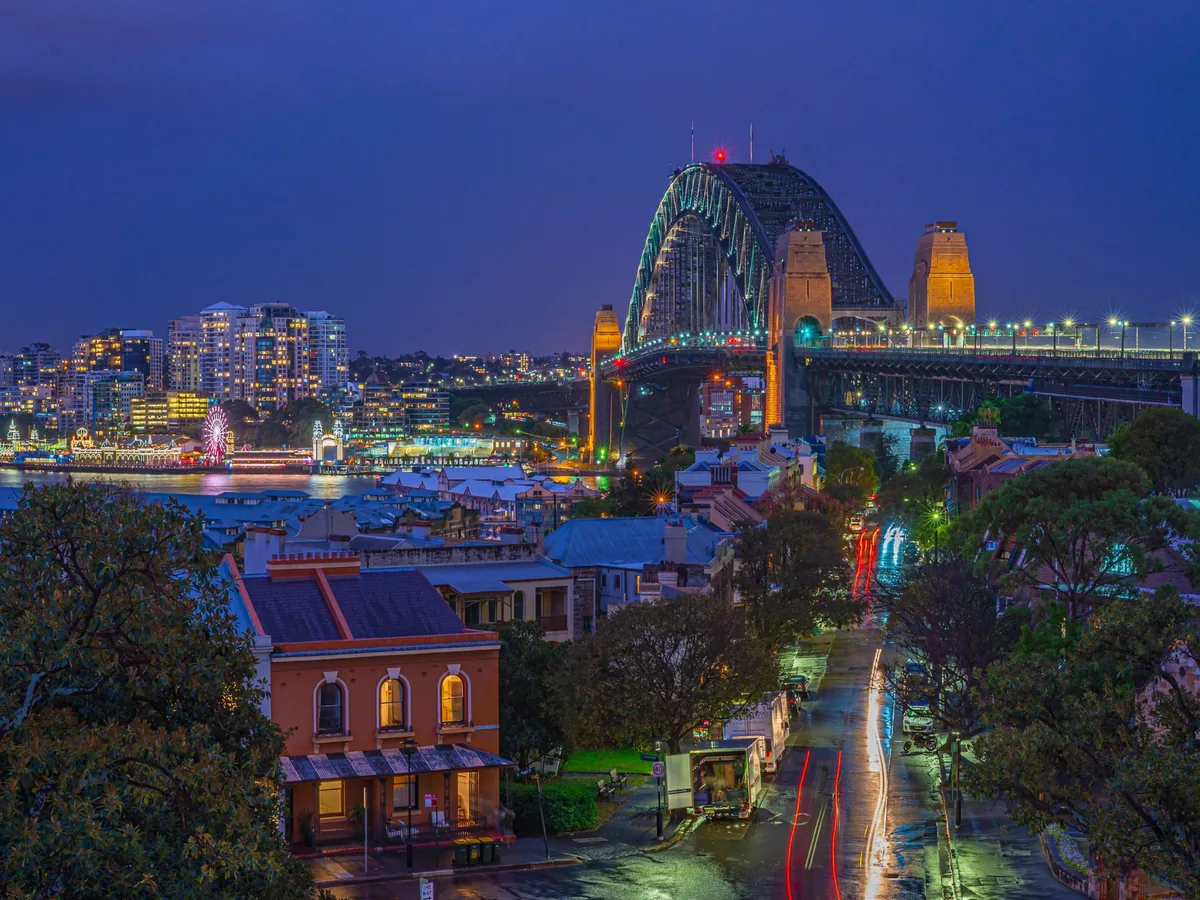 Sydney Harbour Bridge and Luna Park illuminated beneath a deep blue twilight sky with wet-street reflections