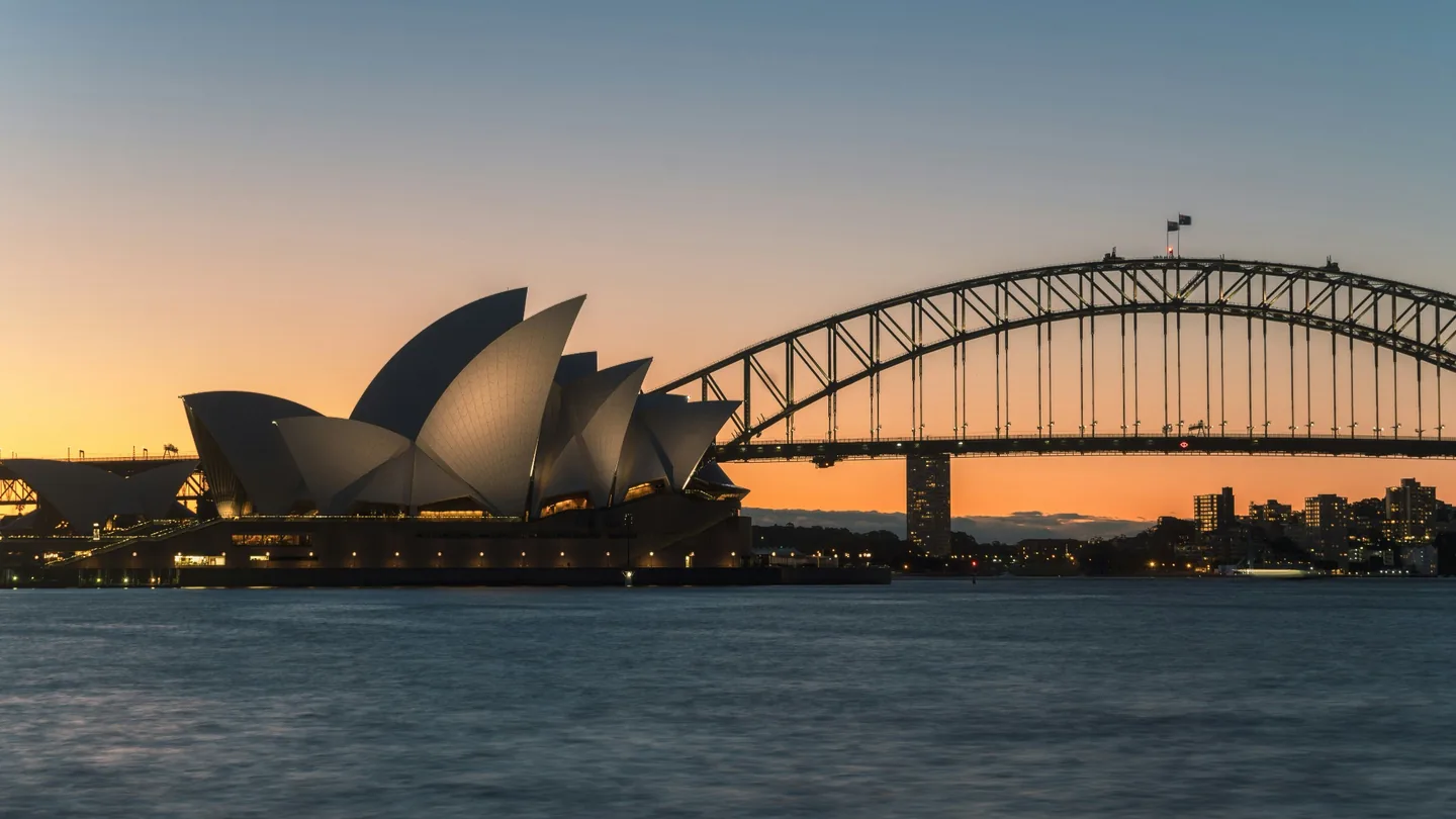 Sydney Opera House and Sydney Harbour Bridge silhouetted against warm sunset light across the harbour