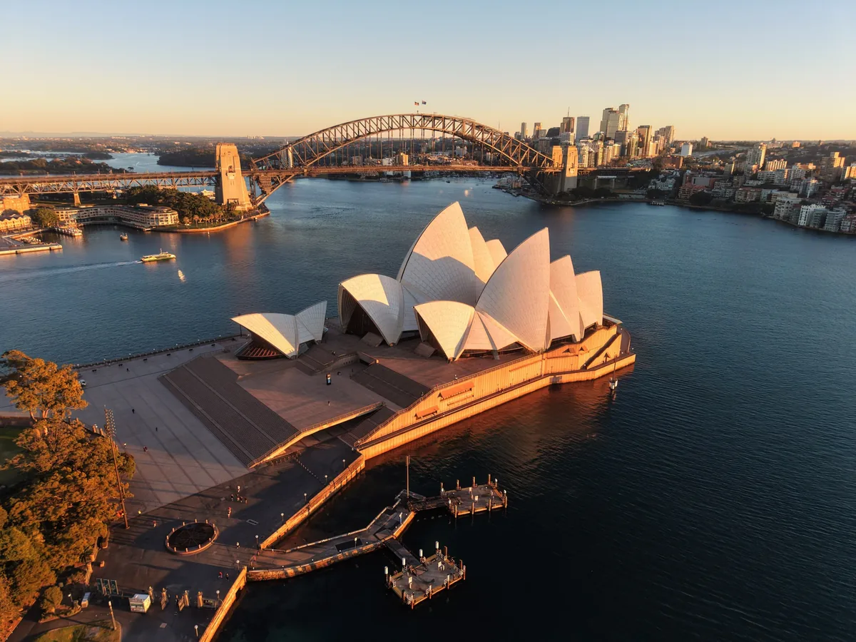 Sydney Opera House illuminated by warm low-angle light with Harbour Bridge and city skyline behind it